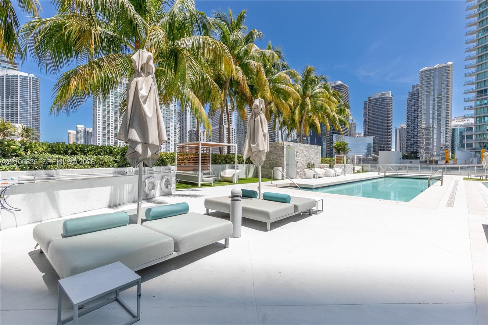 Outdoor pool area featuring a stone-clad wall, manicured palm trees, paved deck, and perimeter landscaping