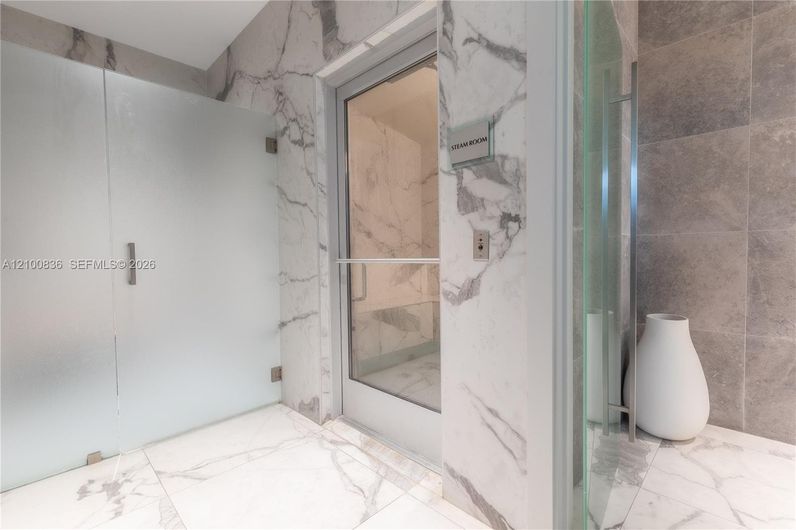 Steam room featuring a glass entry door, floor-to-ceiling stone tile surfacing, and a frosted glass partition