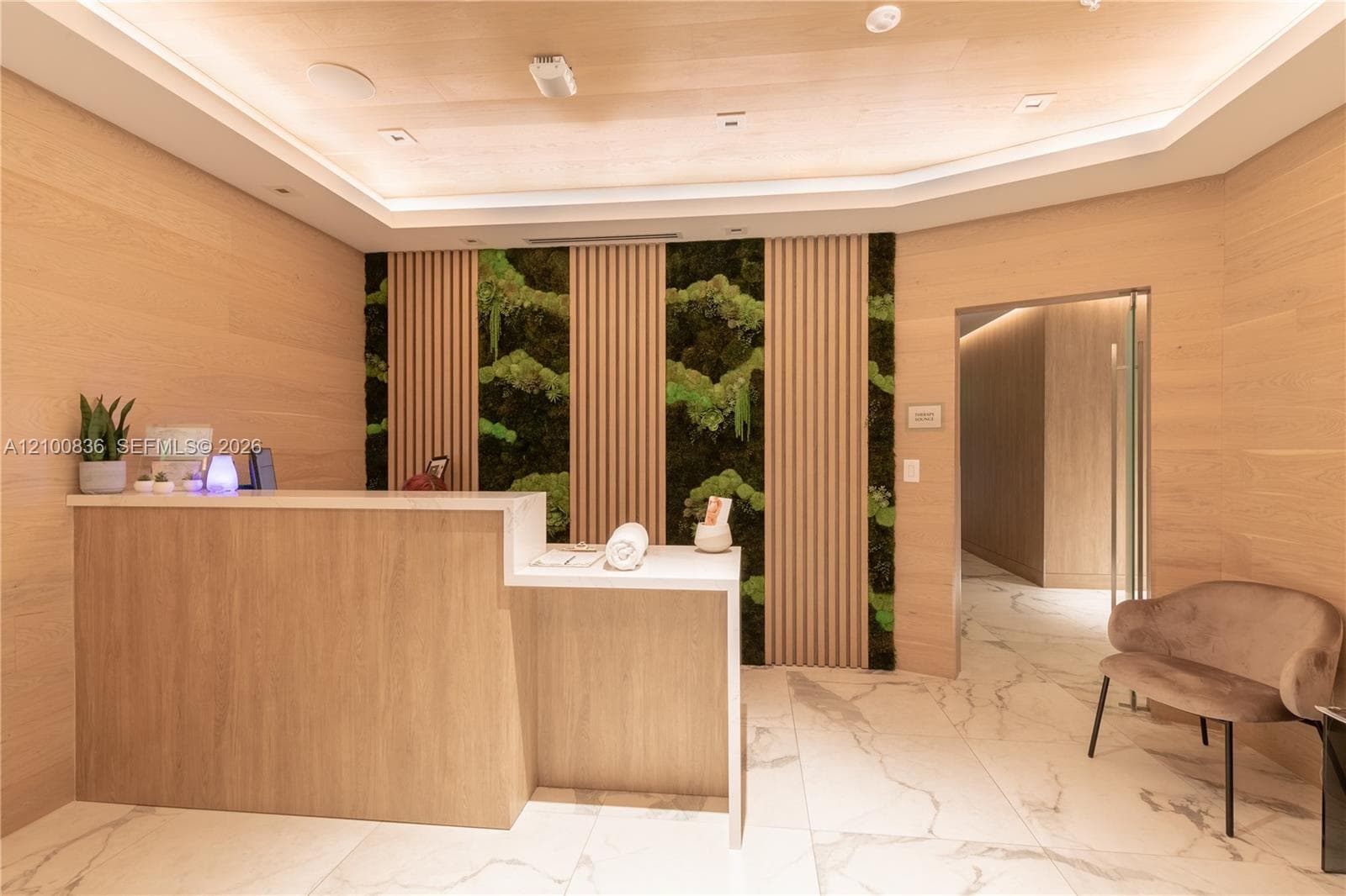 Reception area featuring light wood-finish wall paneling, built-in cabinetry with a stone countertop, vertical slat wood detailing, integrated moss wall panels, and large-format tile flooring
