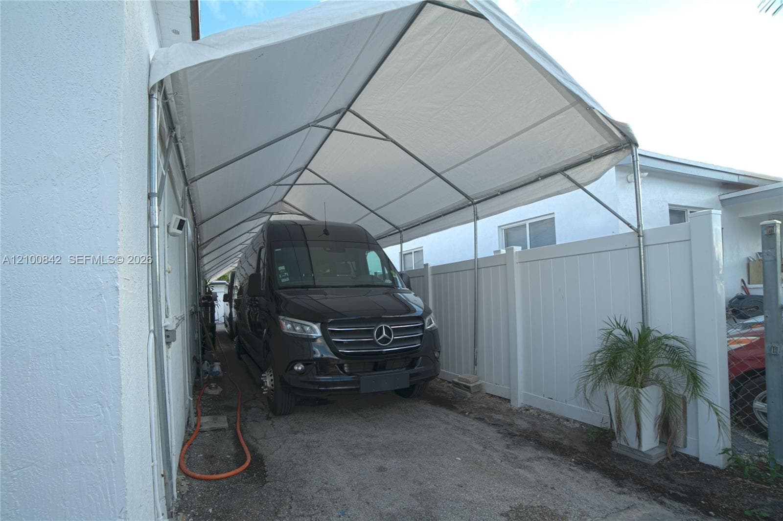 Covered carport structure with a metal frame and weather-resistant canopy, complemented by a white vinyl privacy fence