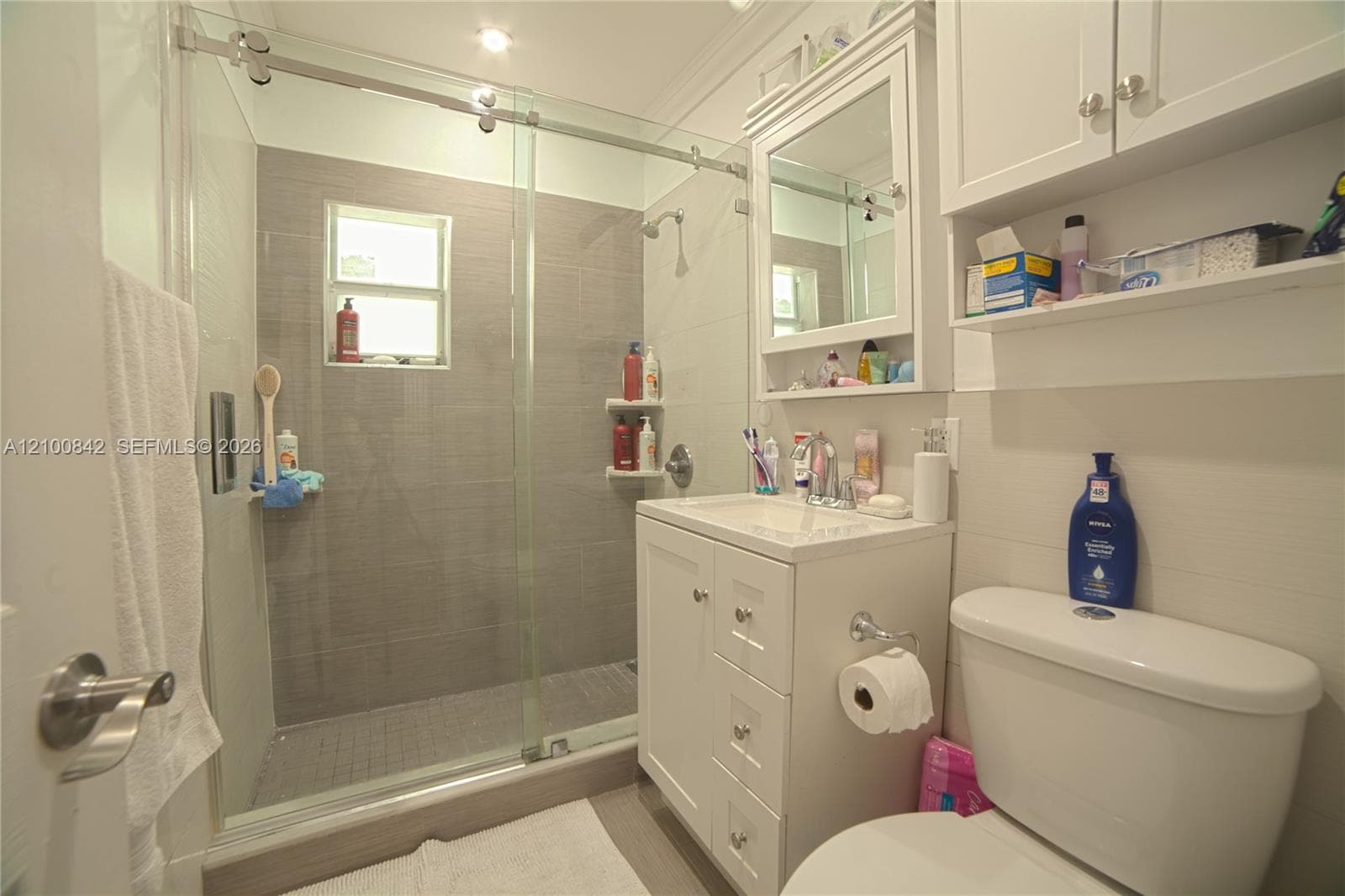 Walk-in shower with sliding glass doors, horizontal tile surround, and built-in shelving, complemented by a white vanity cabinet, integrated medicine cabinet with mirror, and upper cabinetry