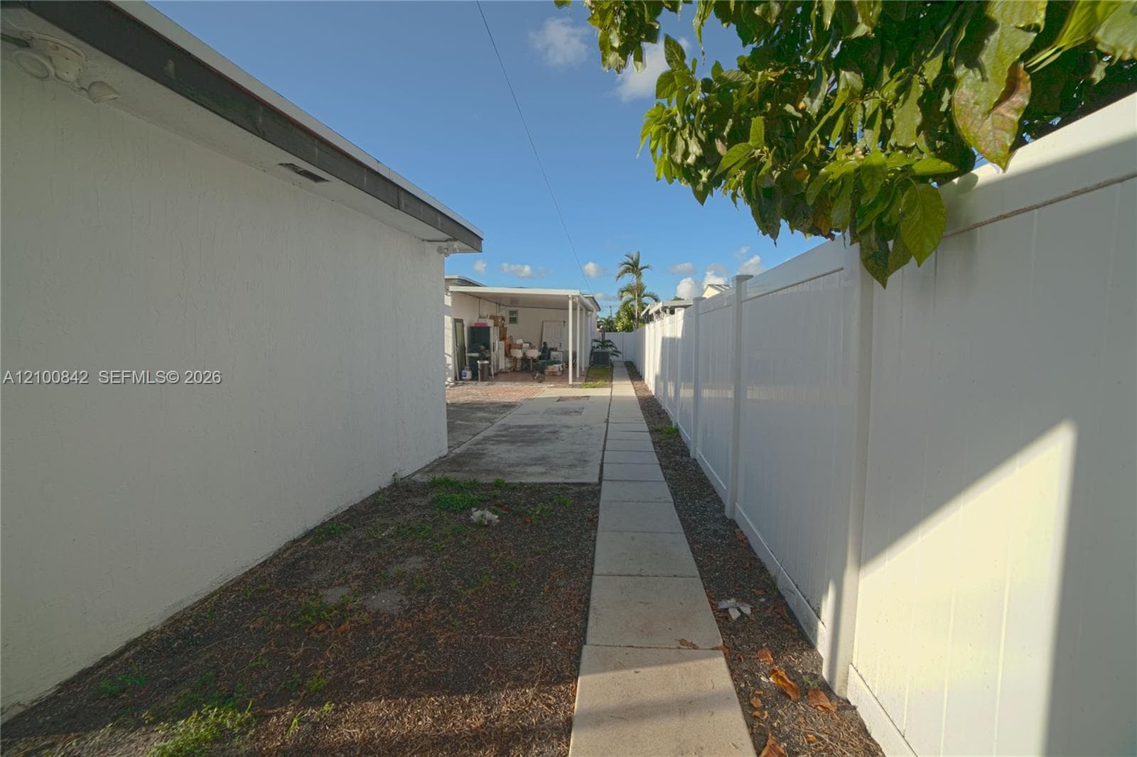 Side yard featuring a concrete paver walkway, white vinyl privacy fencing, and a covered carport area