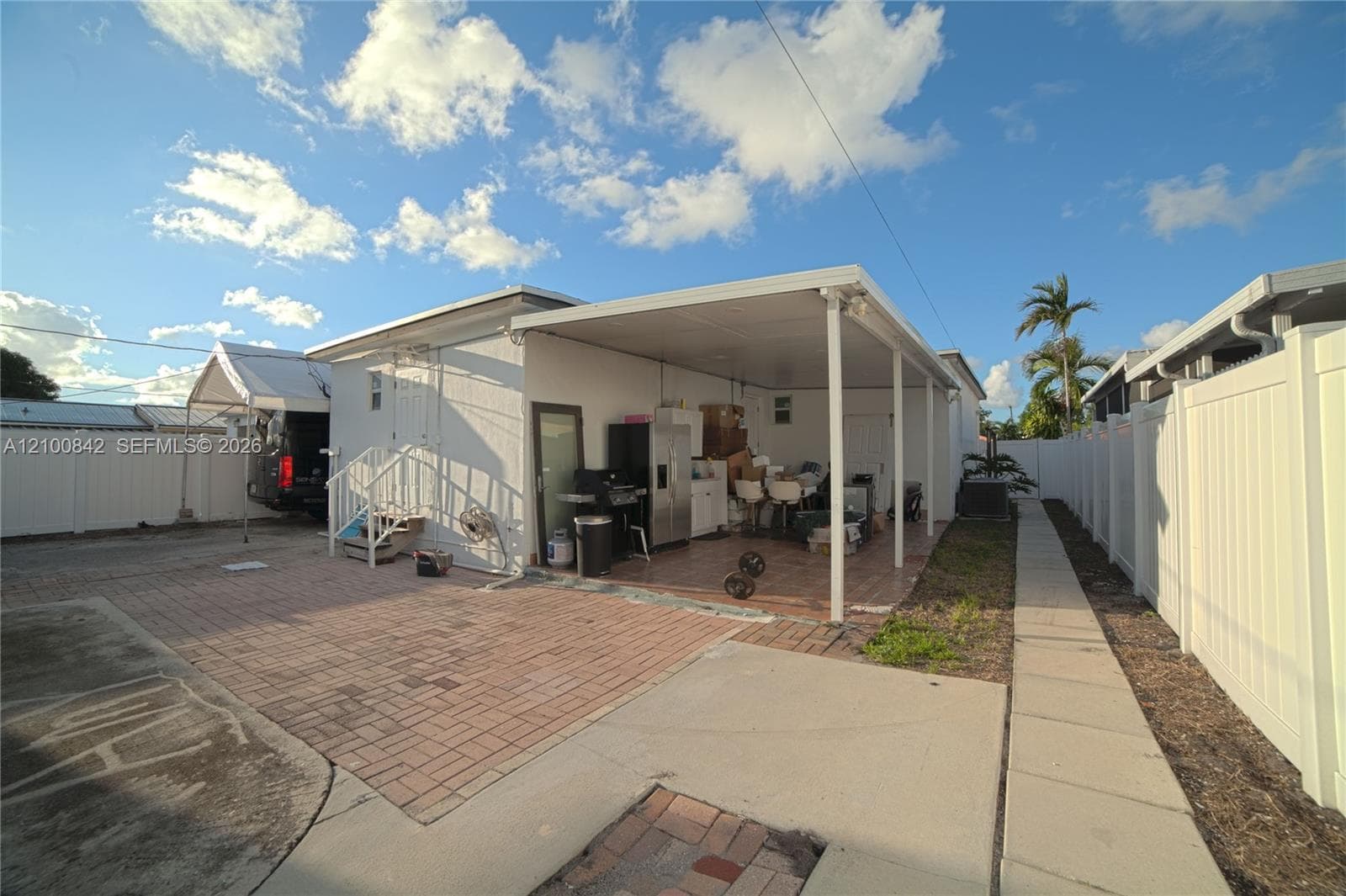 Covered outdoor patio with tile flooring, paver driveway, and white vinyl privacy fencing