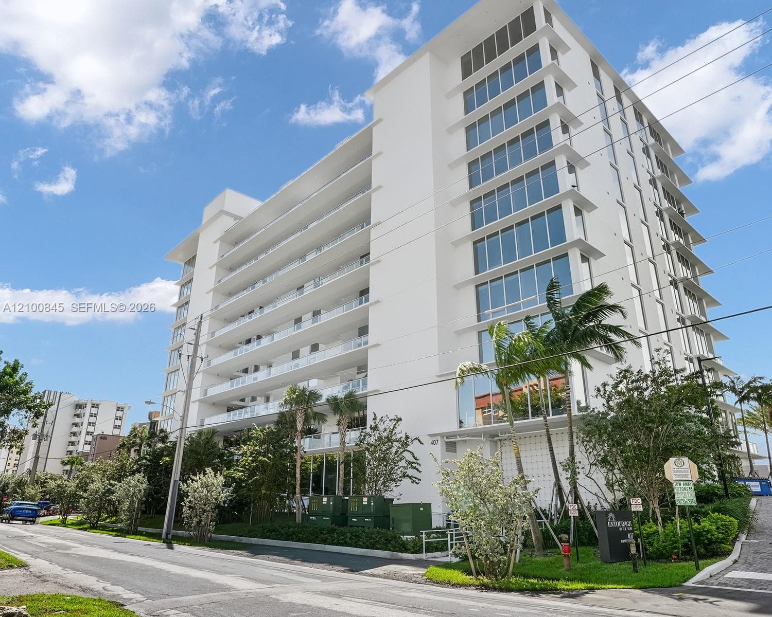 Modern mid-rise building exterior featuring a white stucco facade, expansive glass windows, and multiple stories of private balconies with glass railings