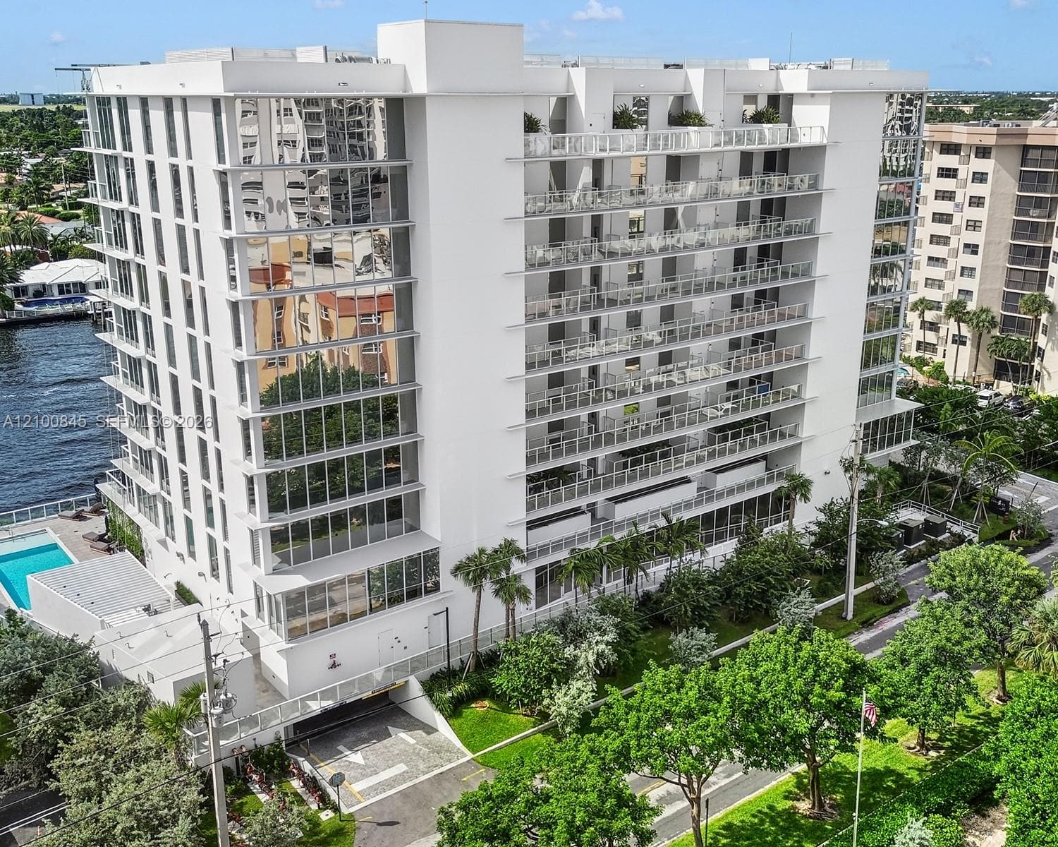Multi-story residential building featuring floor-to-ceiling glass paneling, tiered cantilevered balconies with glass railings, an attached swimming pool, and dedicated subterranean parking access