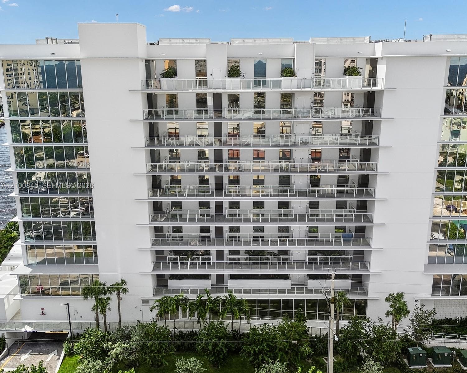 Multi-story residential building exterior featuring floor-to-ceiling glass windows, individual private balconies with glass railings, and incorporated container greenery