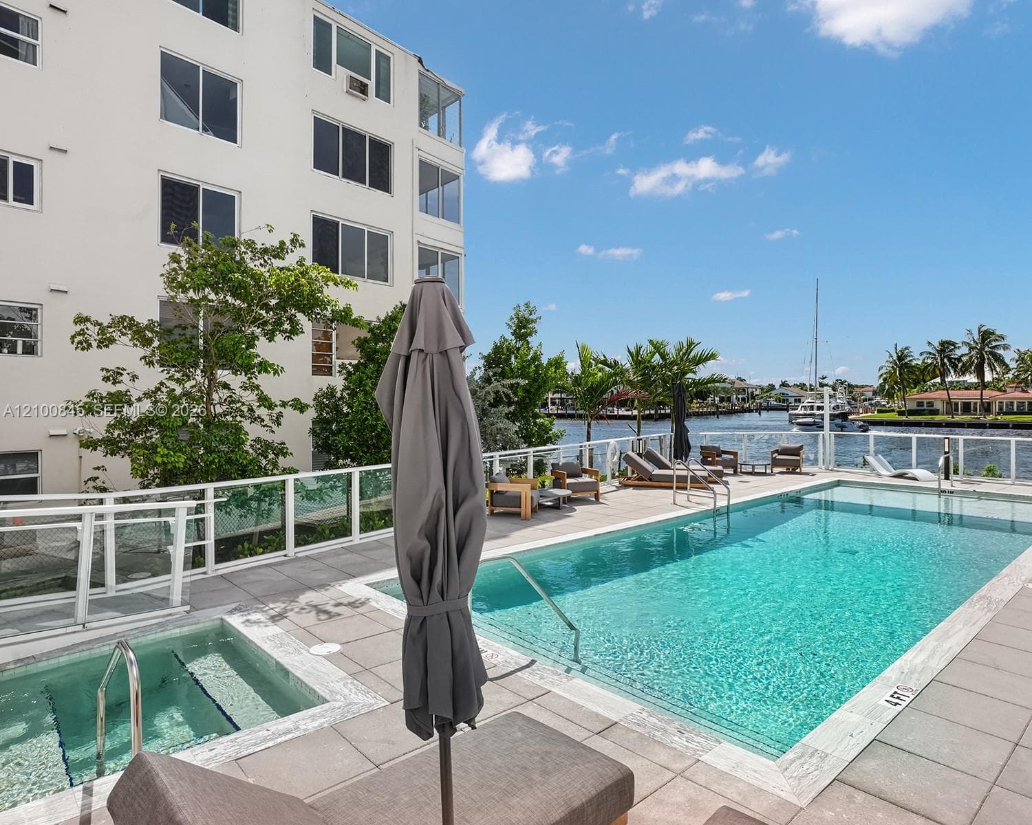 Waterfront pool area featuring a built-in spa, concrete tile decking, and a glass-paneled safety railing