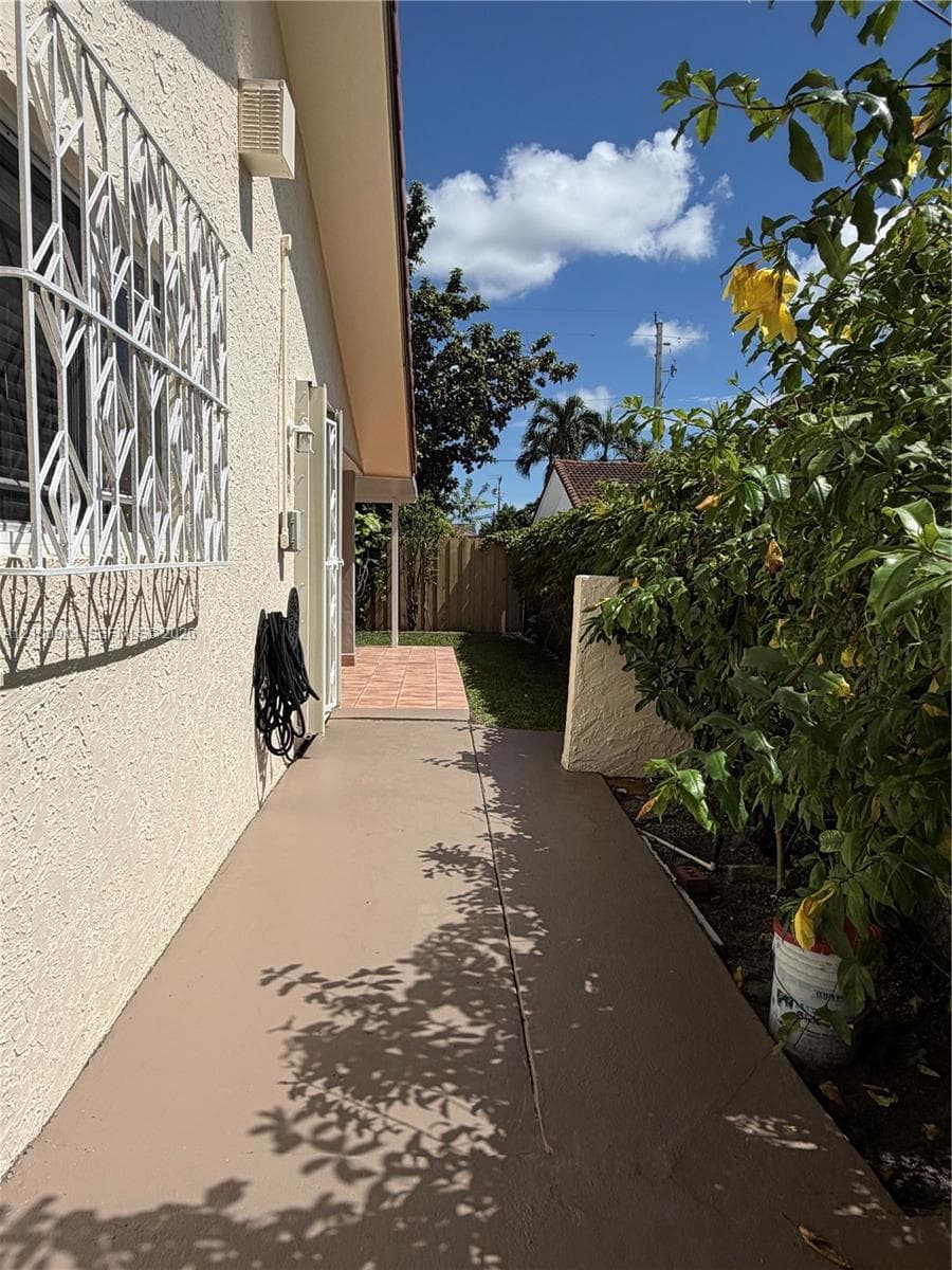 Stucco exterior featuring metal security bars, painted concrete walkway, tiled patio area, and perimeter wood fencing