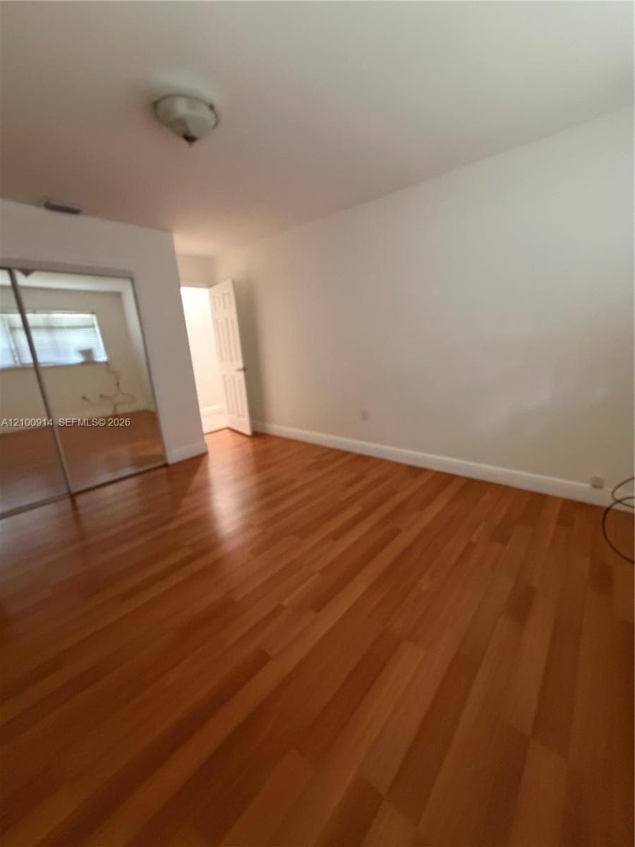 Room featuring wood-finish flooring, sliding mirror-panel closet doors, and a paneled interior door