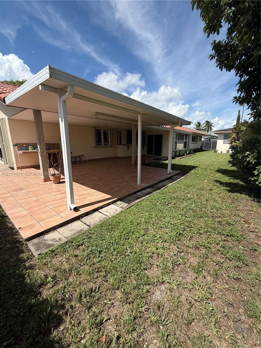 Covered rear patio featuring tile flooring, a built-in outdoor counter, and a expansive lawn