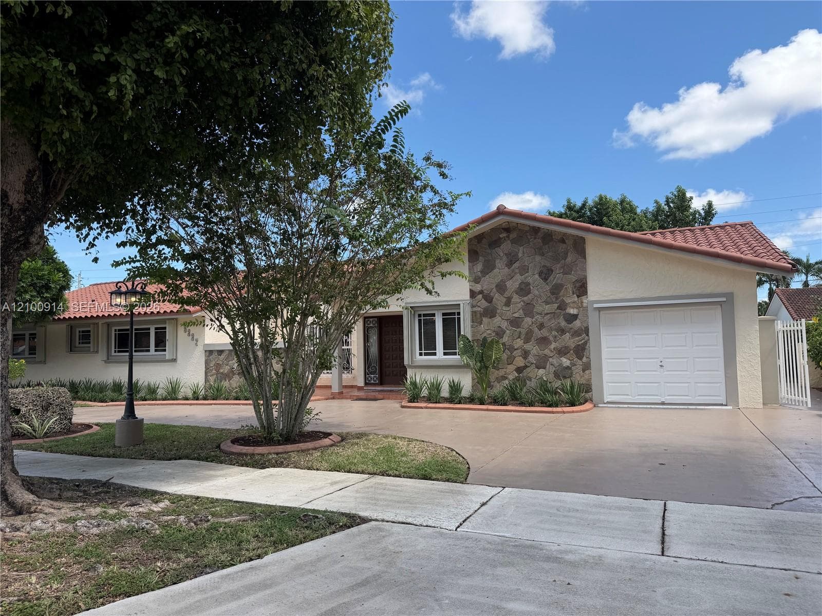 Exterior featuring a stucco facade with stone masonry accents, a tiled roof, a multi-car garage, and a concrete driveway