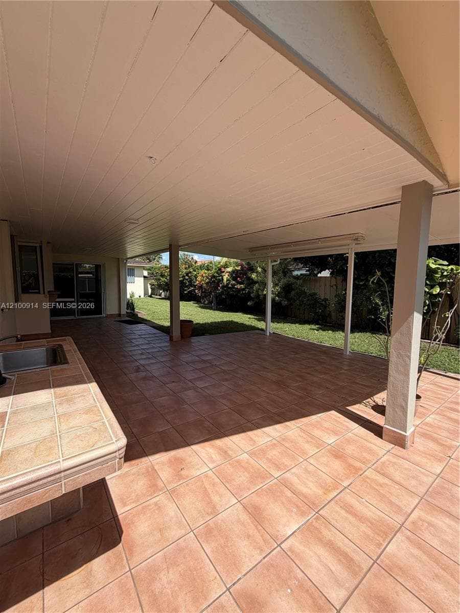 Covered patio featuring ceramic tile flooring, a built-in outdoor counter with integrated sink, and structural support pillars overlooking the lawn