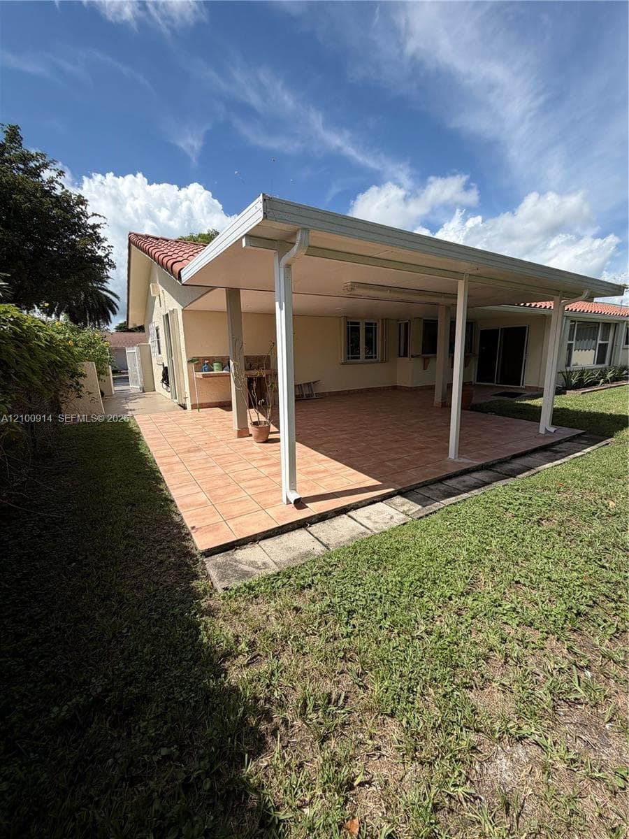 Covered rear patio featuring terracotta-style tile flooring, a built-in outdoor prep counter, and a light-colored stucco exterior