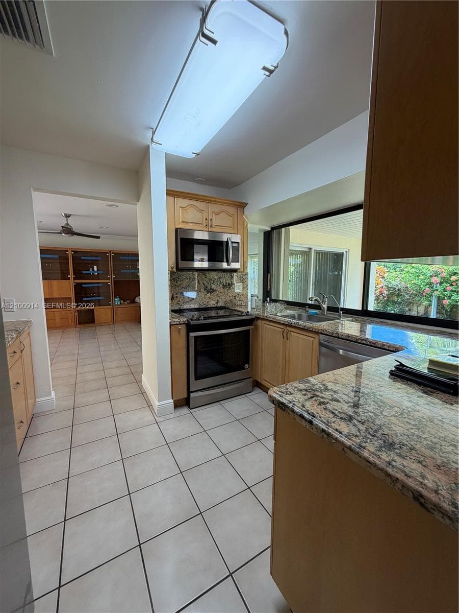 Kitchen featuring light-finish wood cabinetry, stone countertops, stainless steel appliances, tile flooring, and a large horizontal window
