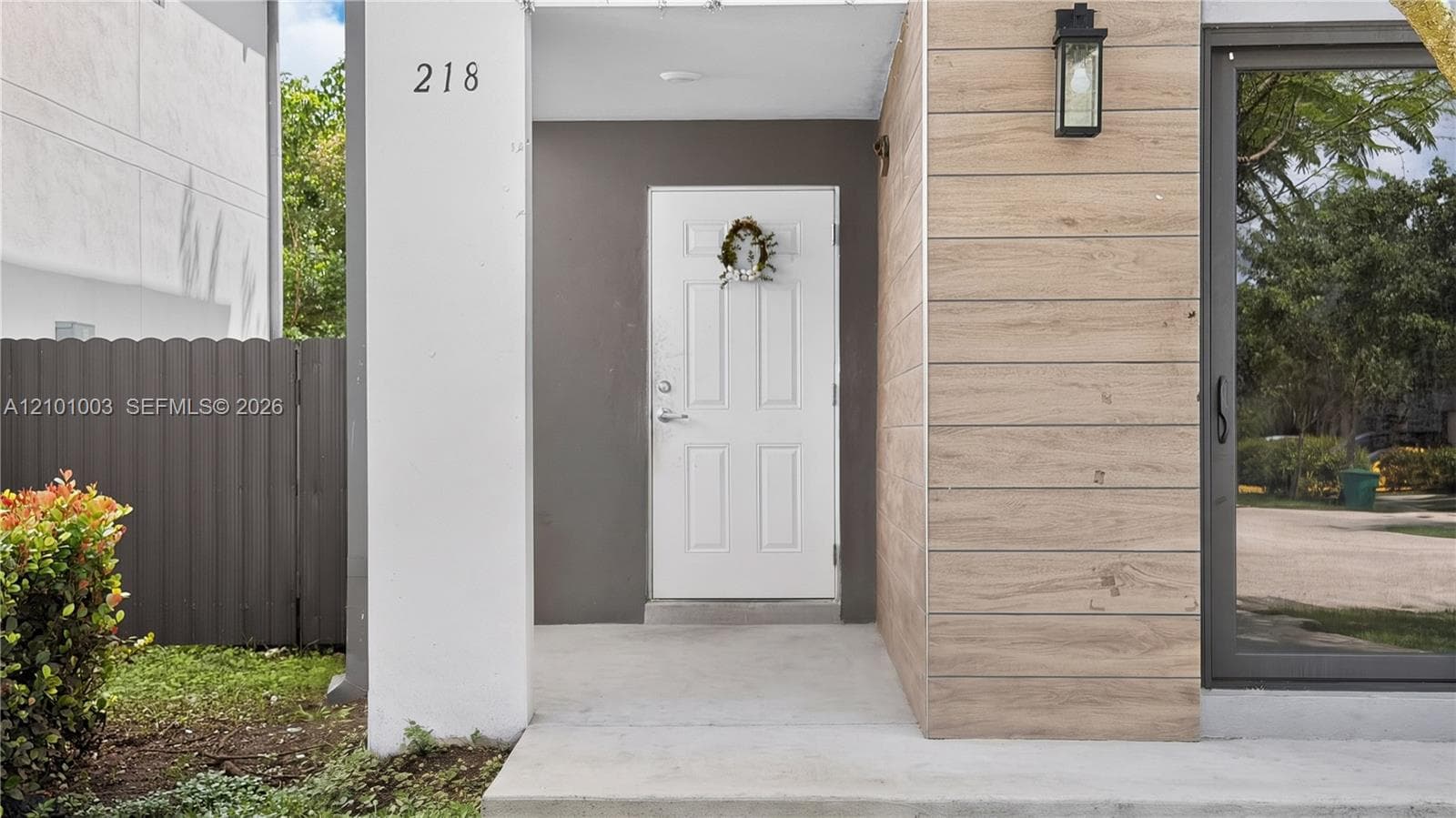 Entryway featuring wood-finish horizontal plank siding, a solid panel door, concrete porch, and rectangular wall-mounted exterior lighting