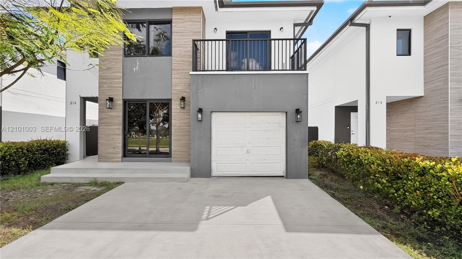 Modern exterior featuring mixed-material facade, private balcony with black railing, single-car garage, and concrete driveway