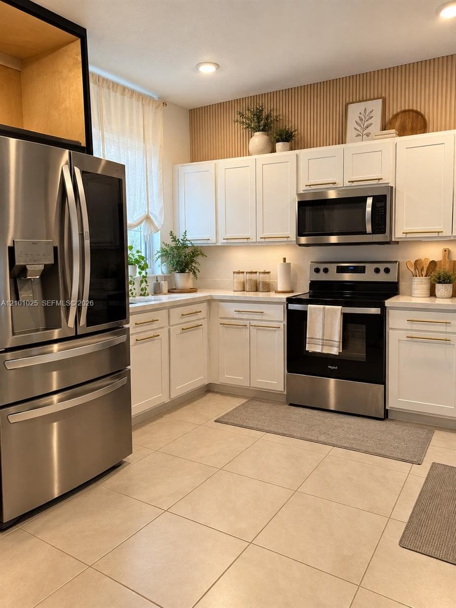 Kitchen featuring white shaker-style cabinetry, stainless steel appliances, vertical slat wall paneling, and tile flooring