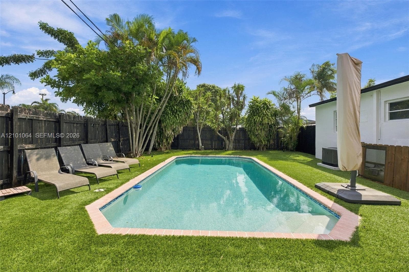 Rectangular in-ground swimming pool featuring a brick-style coping, artificial turf lawn, and perimeter wood privacy fencing