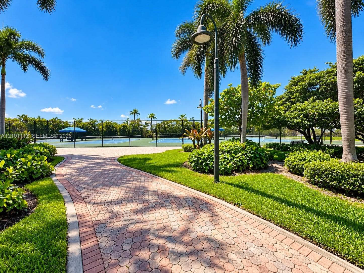 Hardscaped paver walkway featuring manicured landscaping, perimeter fencing, and a fenced court area