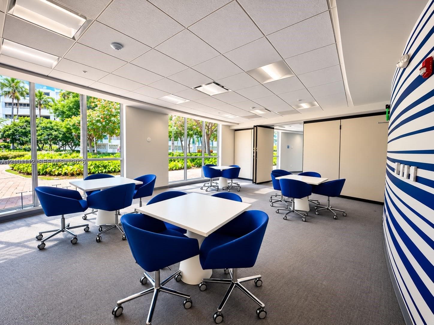 Expansive room featuring floor-to-ceiling windows, recessed drop ceiling lighting, a curved accent wall with a linear pattern, and wall-mounted room dividers
