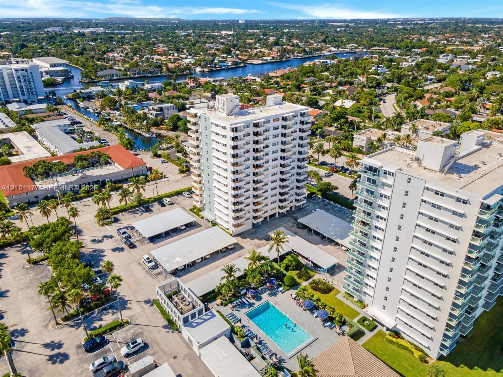 High-rise residential building featuring expansive balcony tiers, an on-site swimming pool, covered parking structures, and manicured landscaping