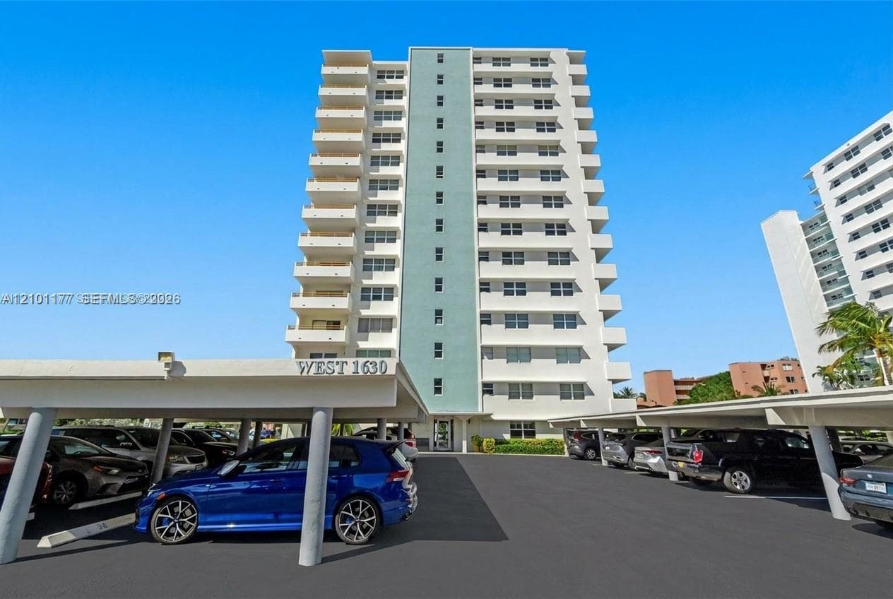 High-rise residential exterior featuring stacked private balconies, a central vertical accent wall, and covered parking structures