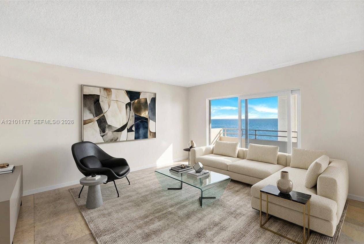Living area featuring stone tile flooring, neutral walls, and a large sliding glass door opening to a private balcony with ocean scenery