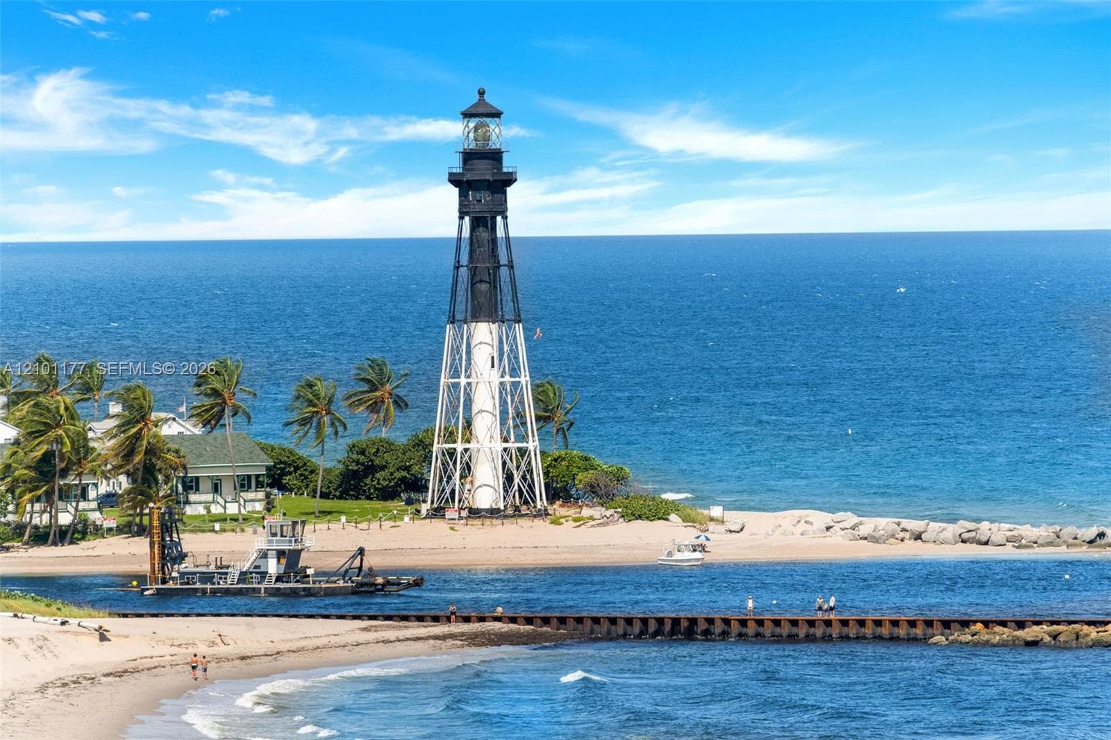 Lighthouse exterior featuring a tapered metal-lattice structure, open-air gallery, and glass-enclosed lantern room situated on a coastal sand beach