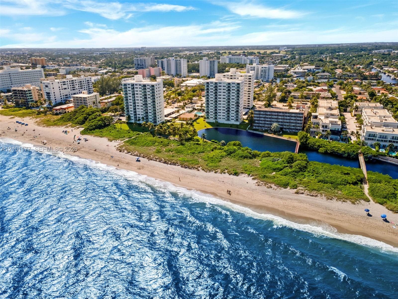 Aerial perspective of oceanfront property featuring sandy coastline, direct water access, and prominent high-rise architecture