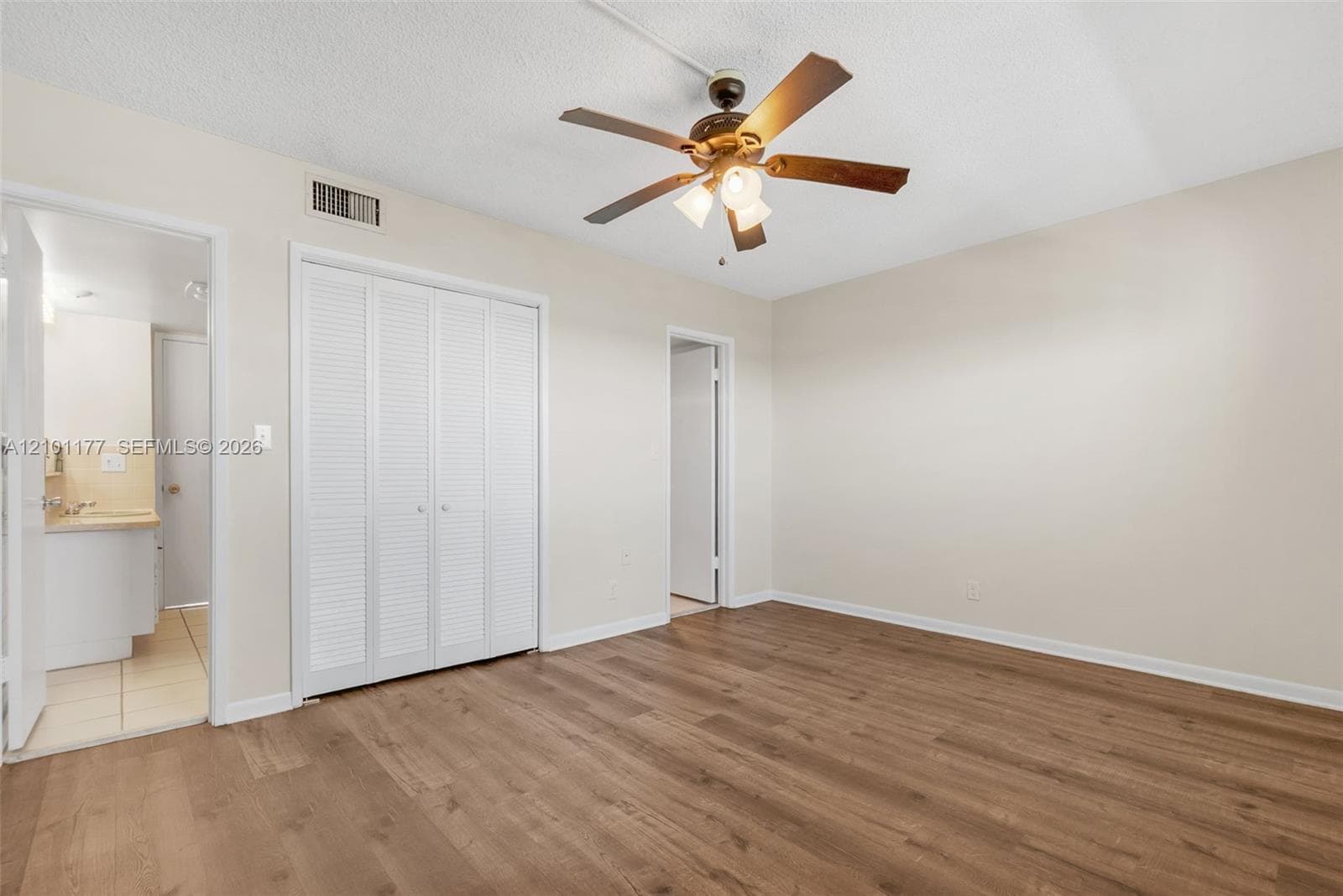 Room featuring wood-finish flooring, a ceiling fan with light fixture, and floor-to-ceiling louvered bi-fold closet doors