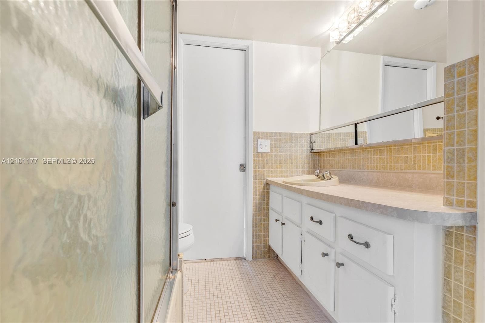 Bathroom featuring white cabinetry, a single-basin vanity, tiled backsplash, large wall-mounted mirror, and a glass-enclosed shower