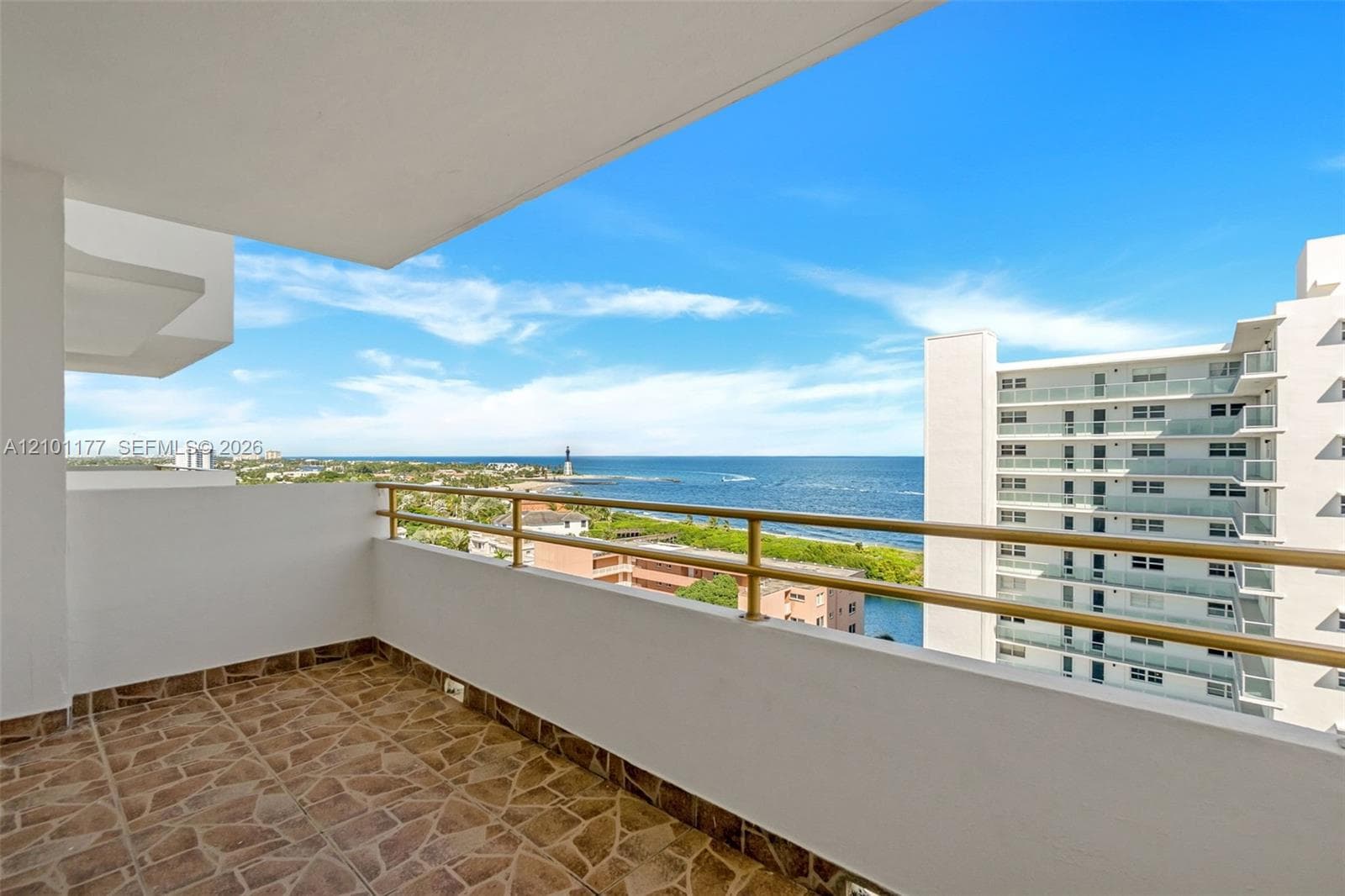 Covered balcony featuring stone-patterned flooring and horizontal metal railing overlooking the ocean and coastline