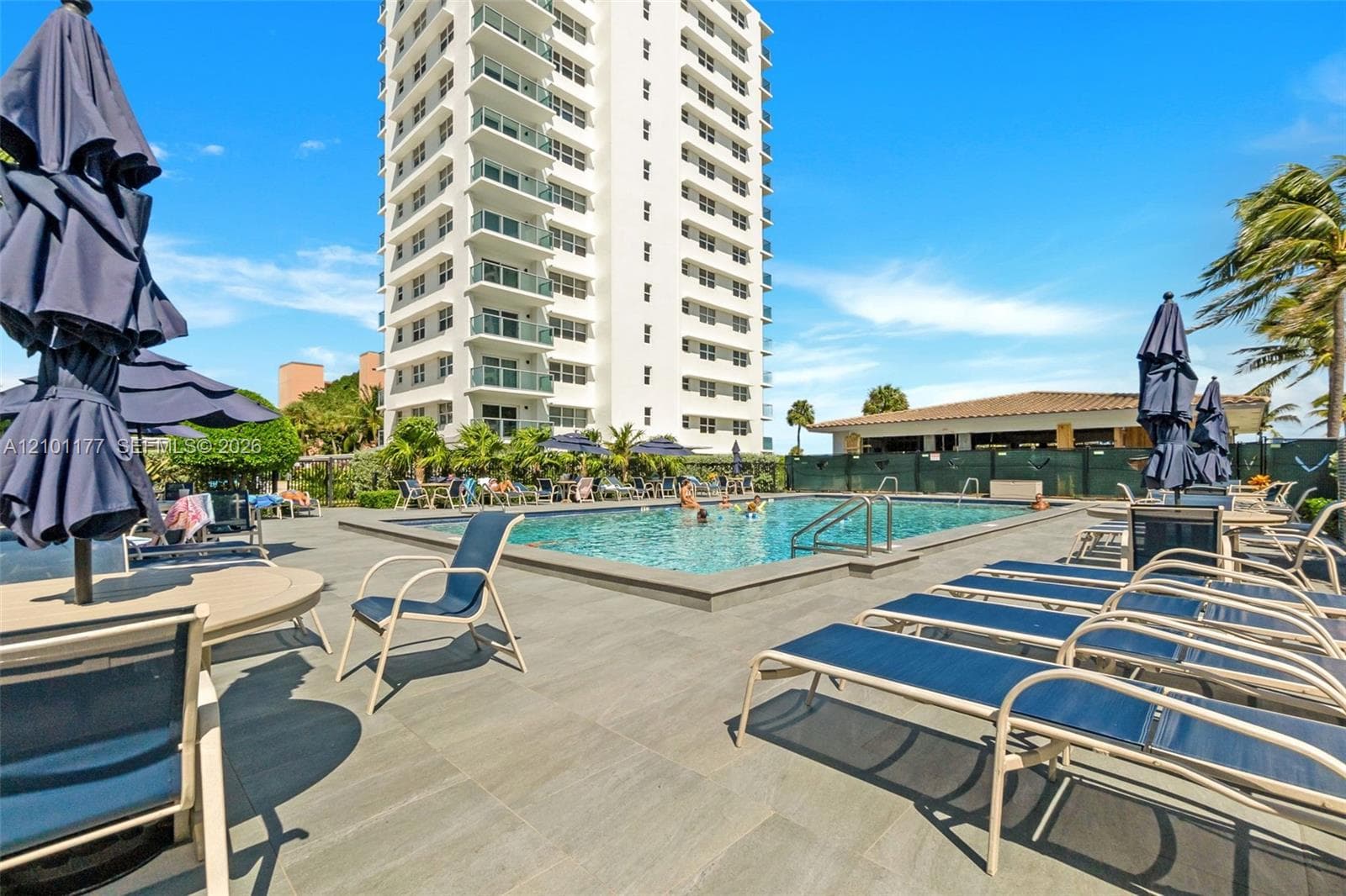 Swimming pool with stone-surfaced patio deck, perimeter privacy fencing, and high-rise exterior structure