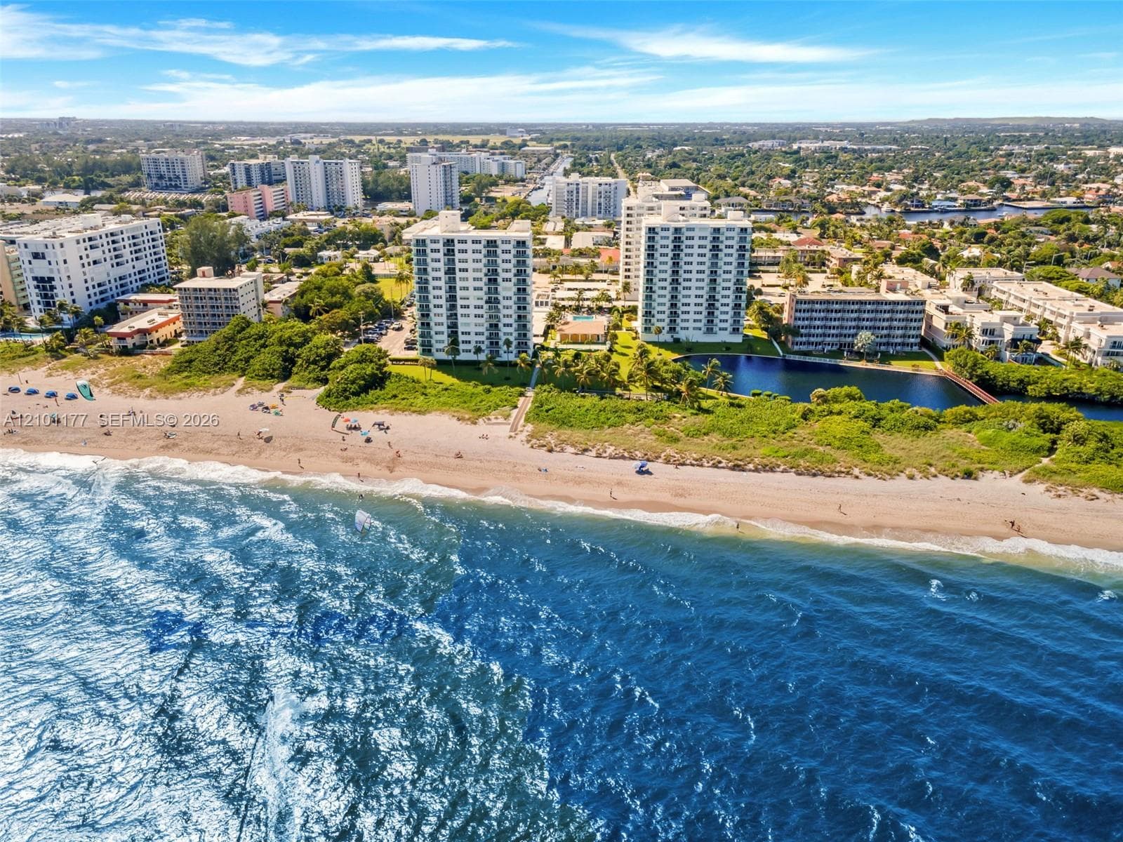 Aerial perspective featuring direct beachfront access, coastal shoreline, and high-rise residential buildings situated on a water feature