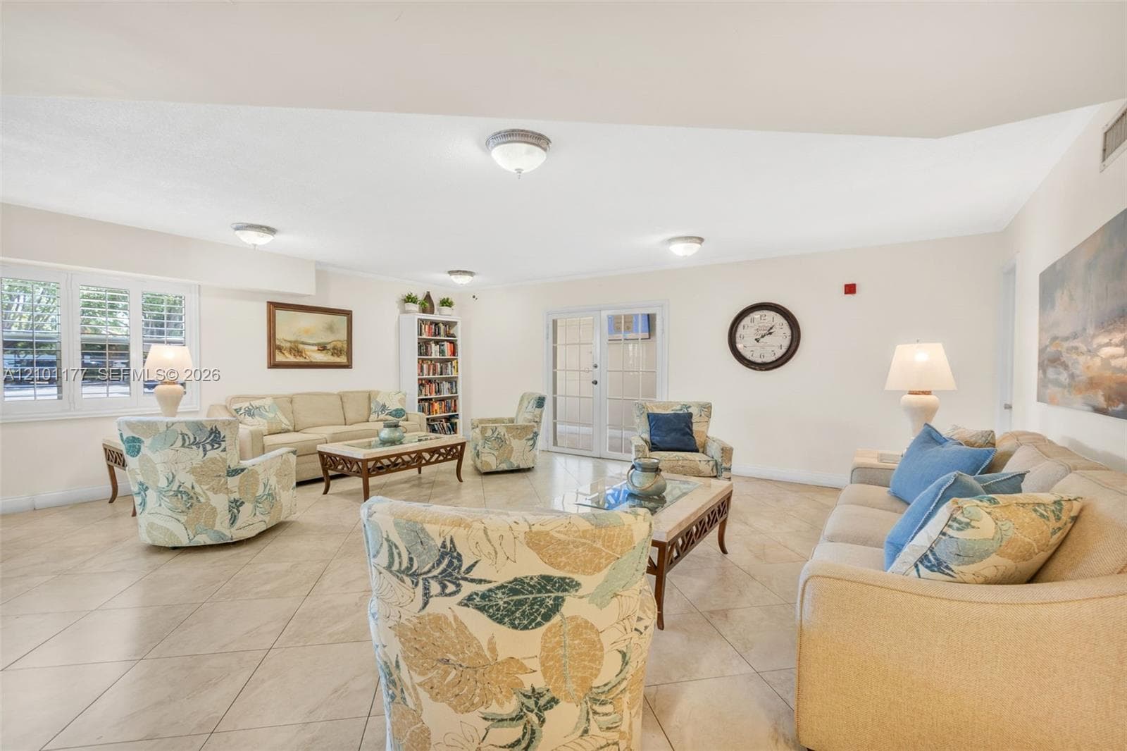 Living area featuring large-format diagonal tile flooring, vaulted ceiling, built-in floor-to-ceiling shelving, triple-panel glass door with grid detailing, and multi-pane windows with plantation shutters