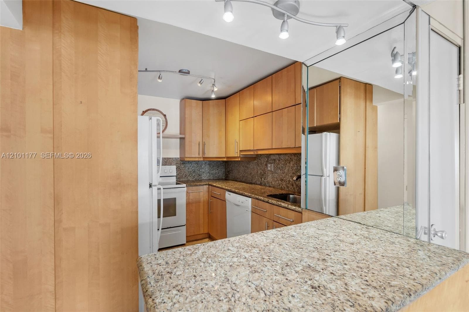 Kitchen featuring wood cabinetry, stone-finish countertops, built-in dishwasher, integrated refrigerator, and multi-directional track lighting