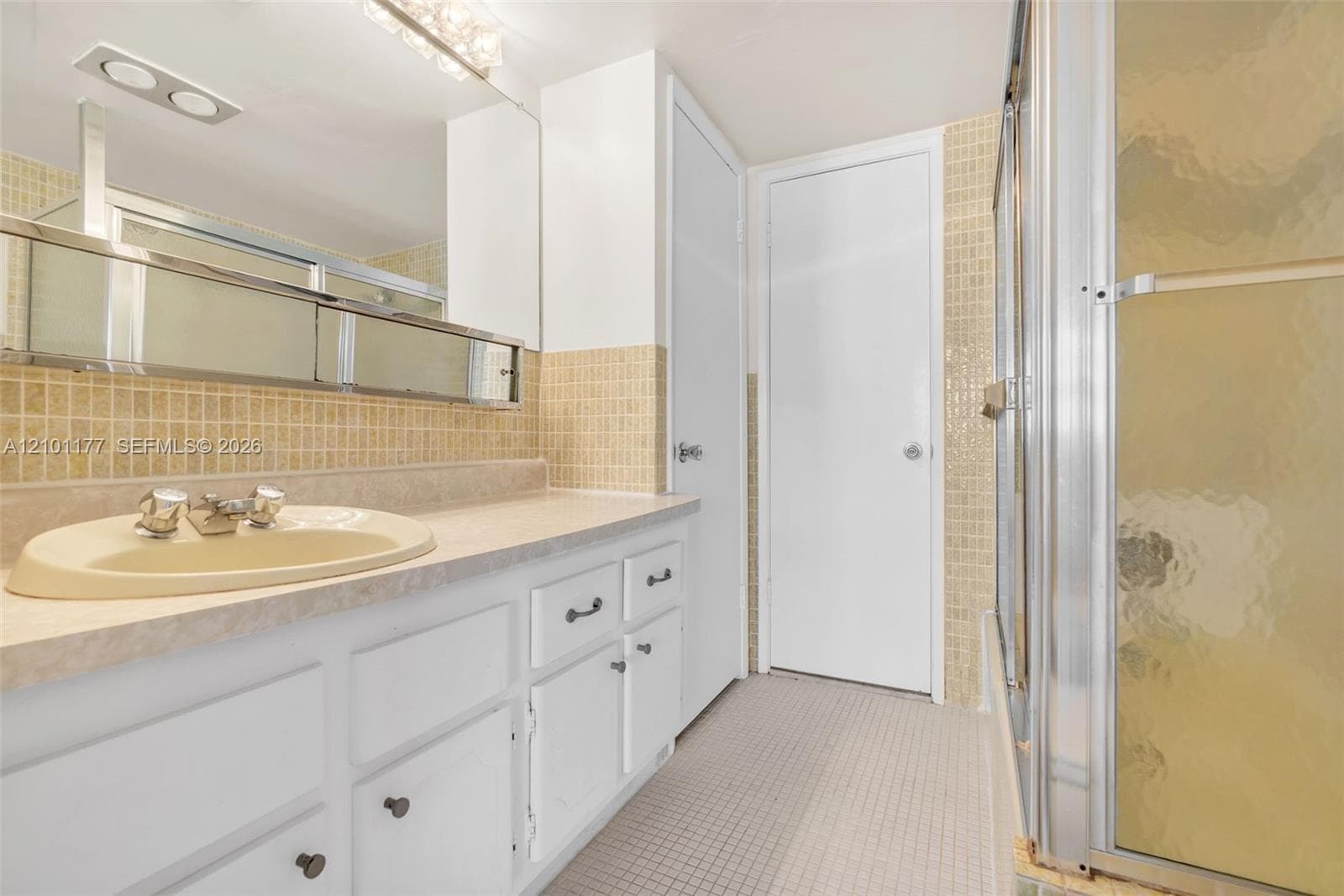 Bathroom featuring a vanity with integrated sink, stone-finish countertop, white cabinetry, tile backsplash, and a glass-enclosed shower