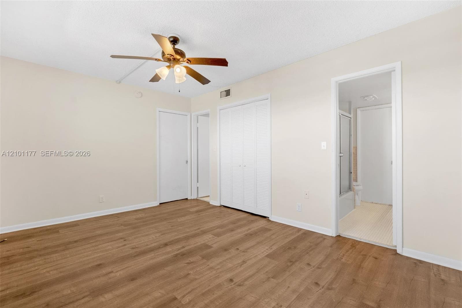 Wood-finish flooring, neutral wall tones, multi-panel closet doors, and an overhead ceiling fan with light fixture