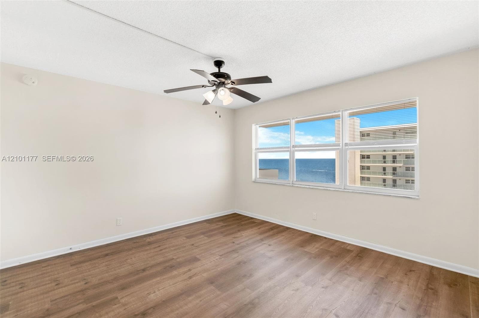 Interior space featuring wood-finish flooring, a multi-blade ceiling fan with integrated lighting, and horizontal sliding windows showcasing ocean scenery