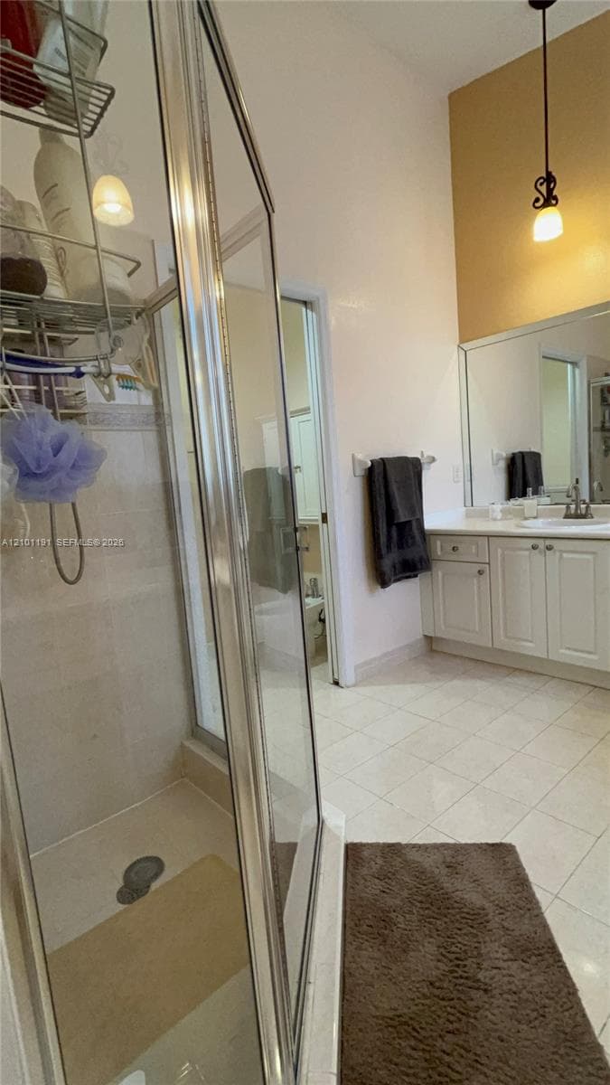 Glass-enclosed shower with tiled surround, white vanity cabinetry, integrated sink, large wall-mounted mirror, and pendant lighting
