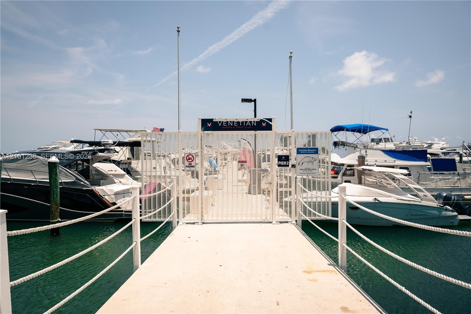 Private marina pier featuring a concrete walkway, white-finish metal security gate, and rope-style railings