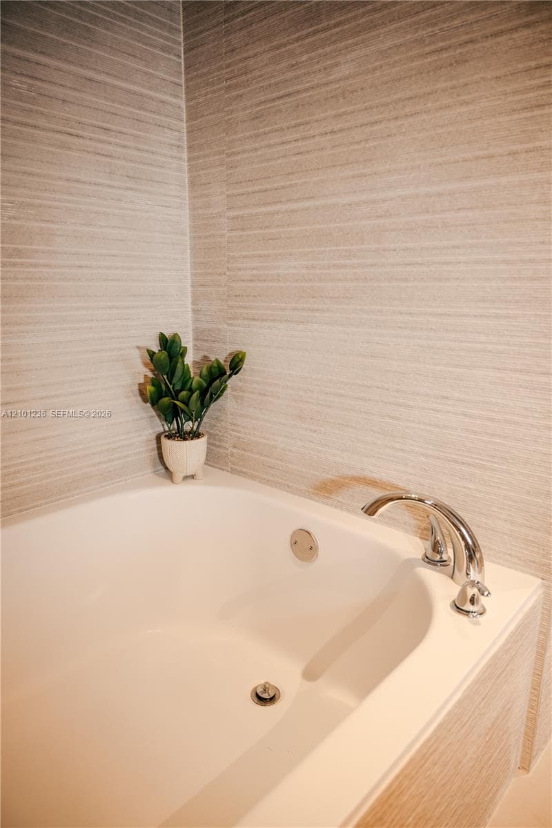 Soaking tub featuring a polished chrome deck-mounted faucet and full-height textured tile surround