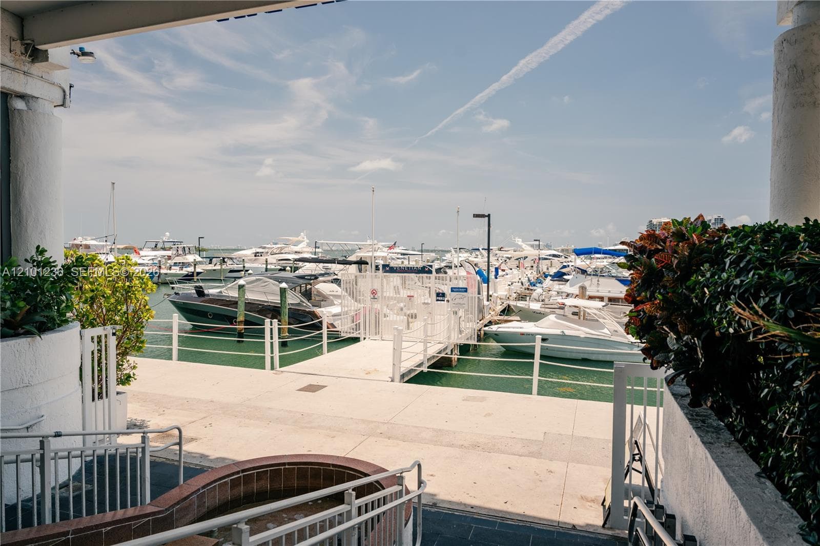 Covered patio featuring concrete flooring, integrated brick-lined planter, metal railing, and direct water access to a private marina