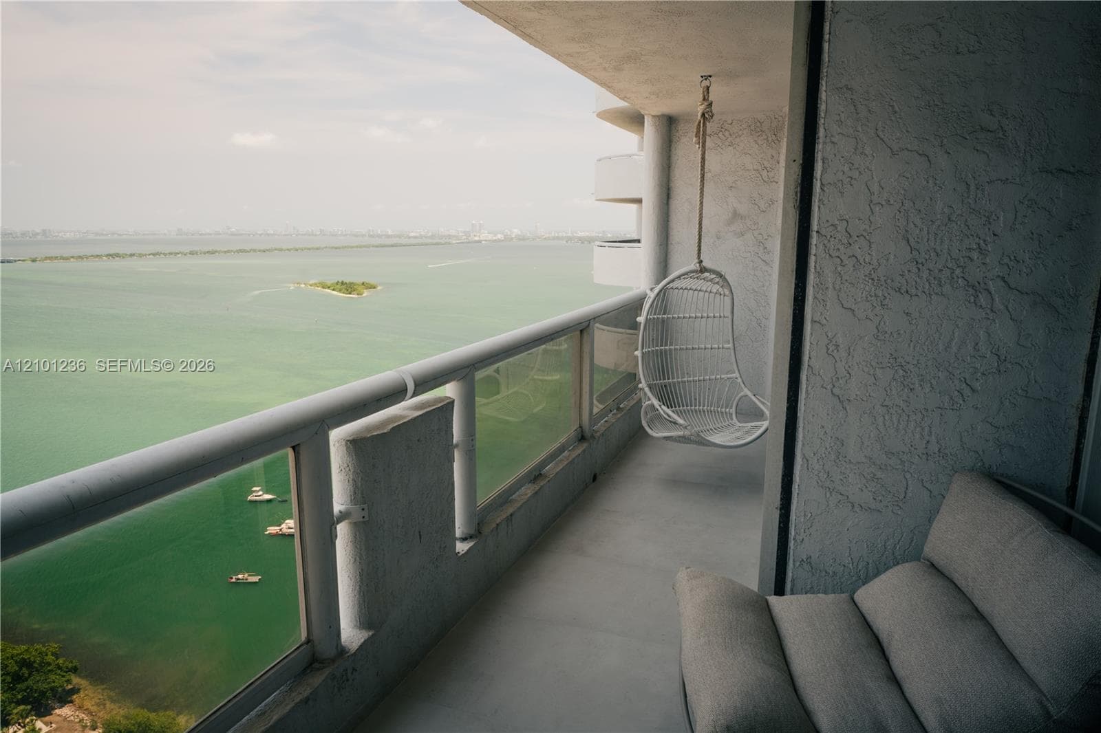 Covered balcony featuring water scenery, textured stucco walls, and a glass-paneled metal railing