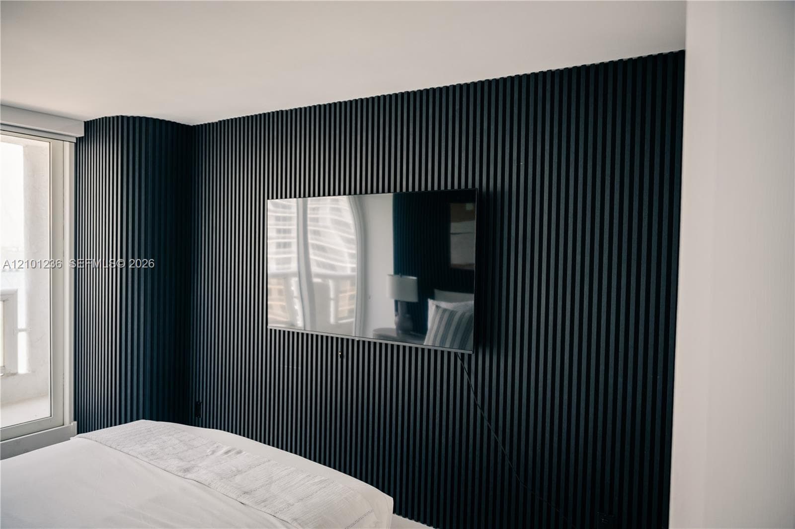 Accent wall featuring matte black vertical slat paneling with a curved corner detail and wall-mounted television bracket