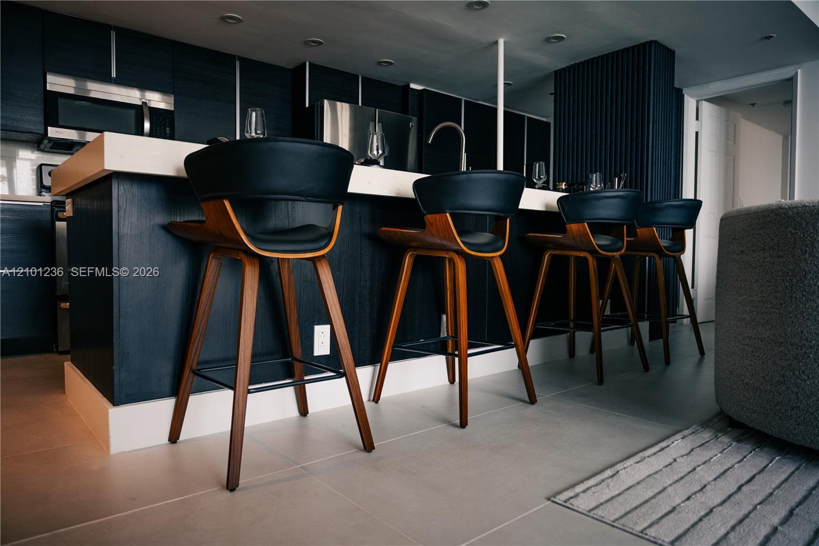 Kitchen featuring dark-finish cabinetry, a waterfall-edge countertop, stainless steel appliances, and large-format tile flooring