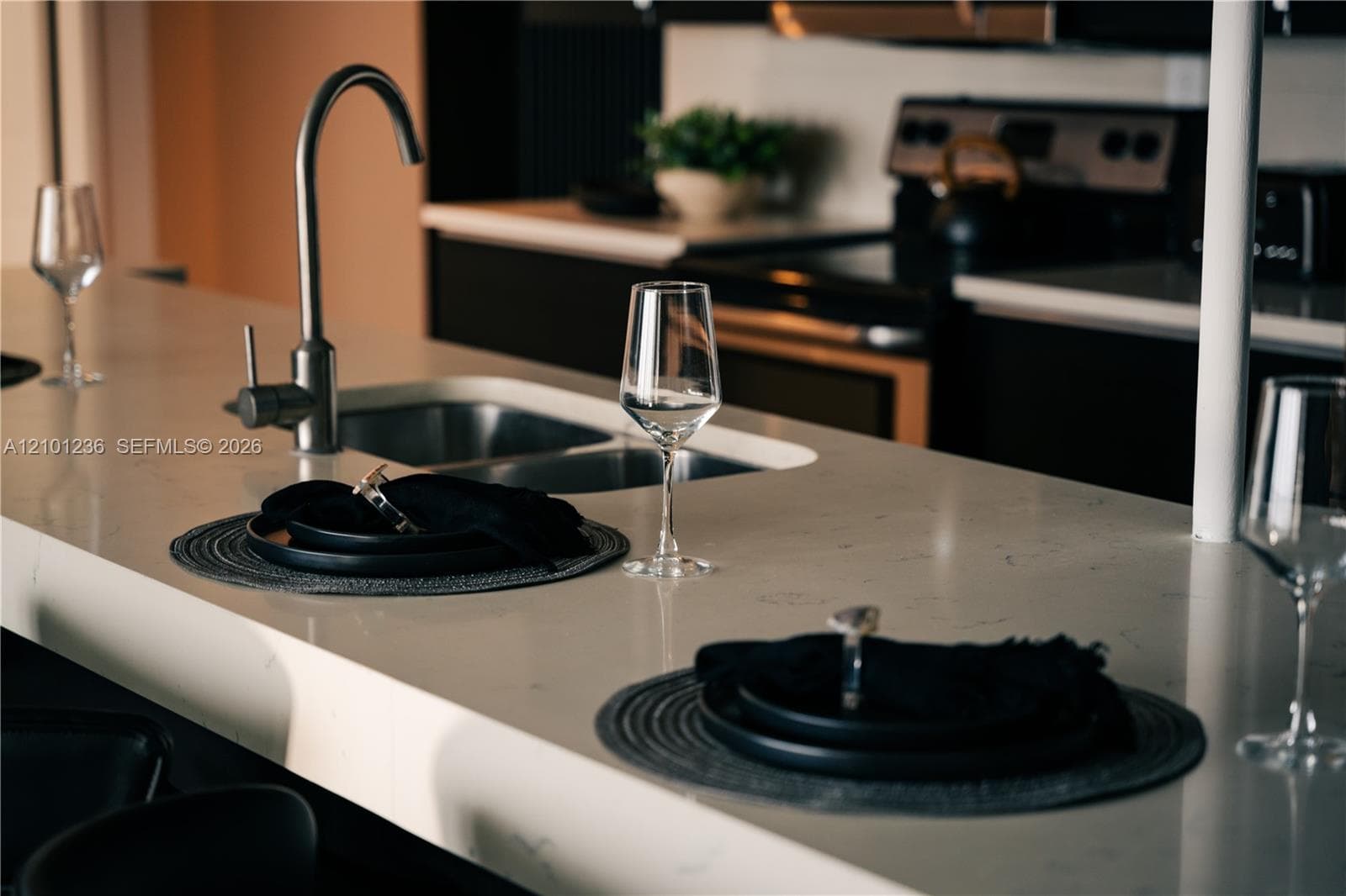 Kitchen island featuring a stone-look countertop, undermount sink, and brushed metal gooseneck faucet, set against dark cabinetry