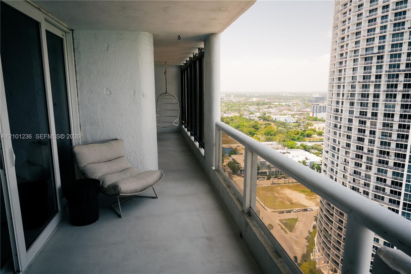 Covered balcony with large-format tile flooring, textured wall finishes, and a full-length metal railing