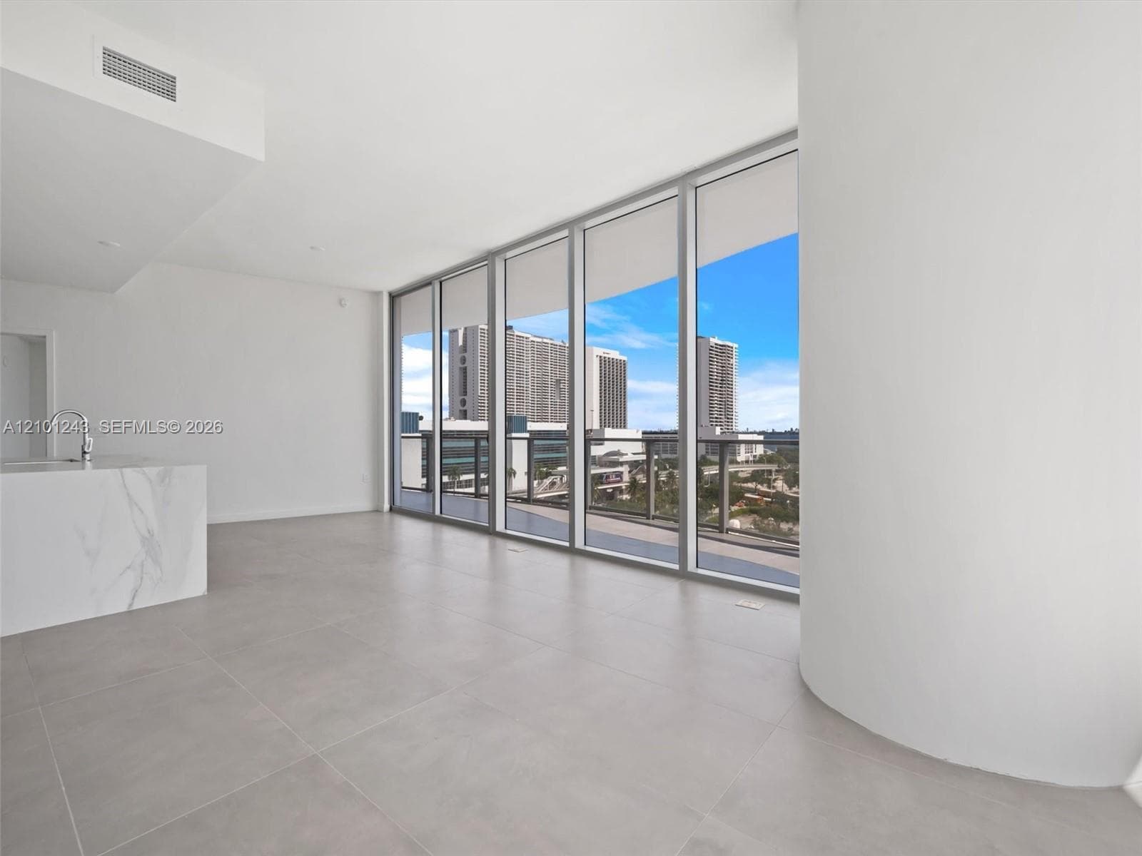 Floor-to-ceiling windows, stone-finish kitchen island, large-format tile flooring, and curved architectural wall