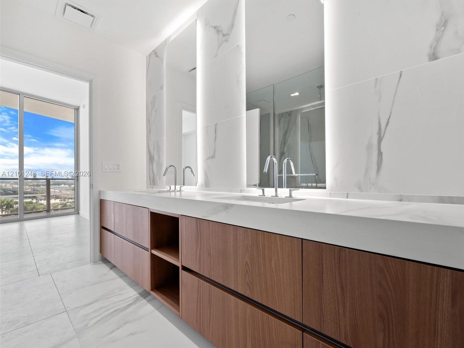 Floating wood-finish vanity with stone countertop, dual integrated sinks, floor-to-ceiling stone wall cladding, and illuminated mirrors